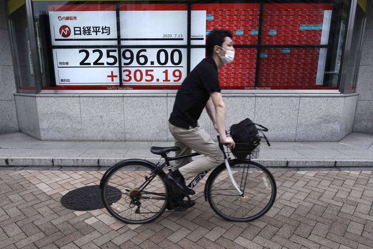 A man wearing a face mask to help curb the spread of the coronavirus rides a bicycle near an el ...