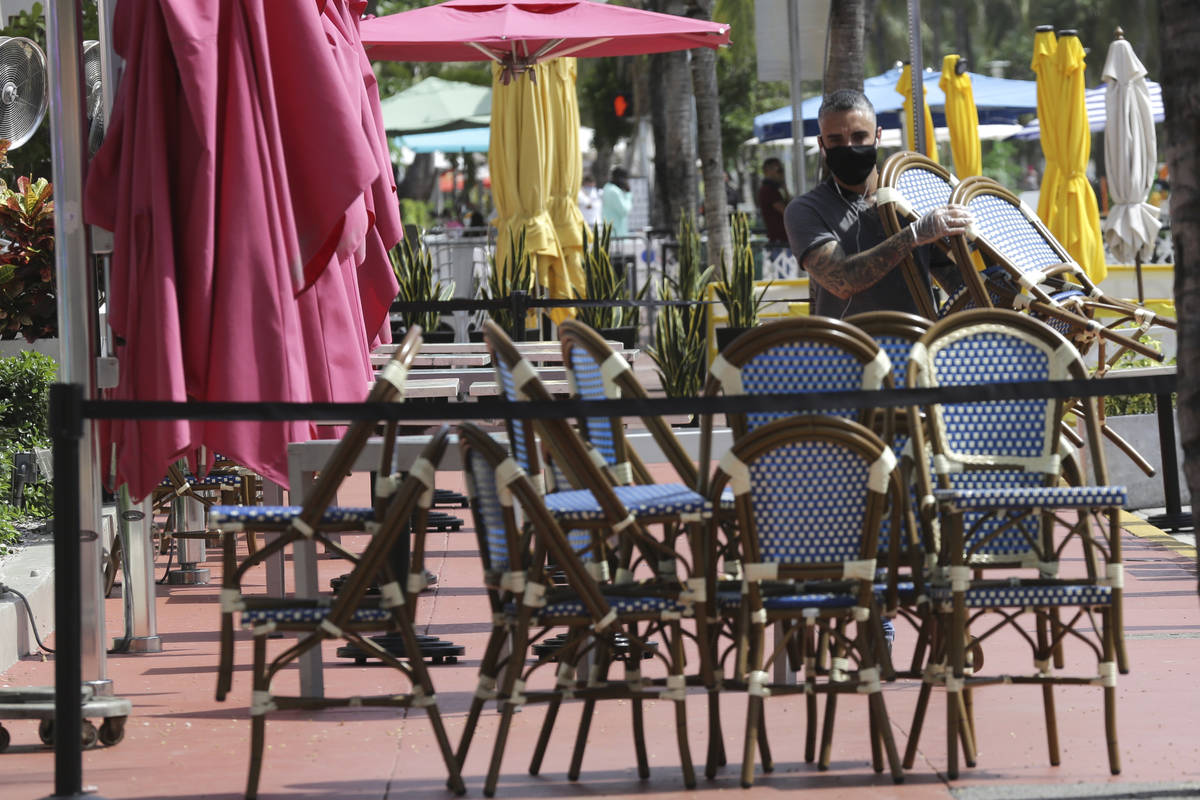 An employee at the Clevelander bar and restaurant on Ocean Drive stacks chairs as they have shu ...