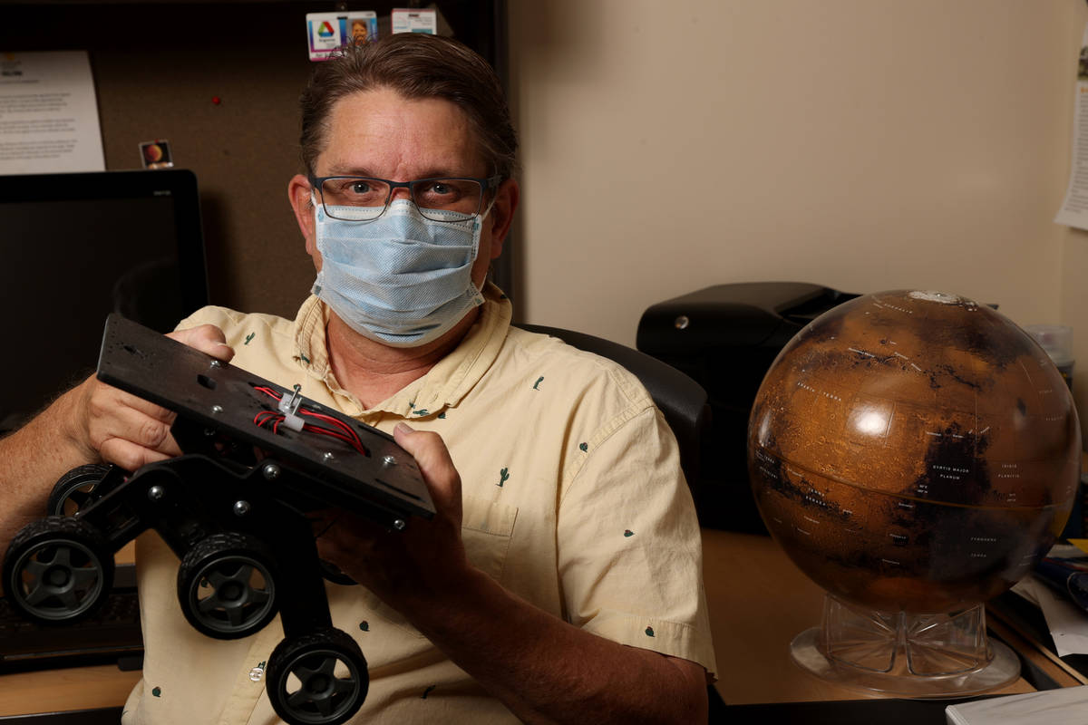 UNLV Professor Christopher Adcock with Mars globe and rover chassis in his office on campus in ...