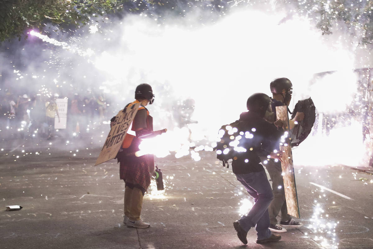 Protesters walk away from crowd control munitions launched by federal officers during a Black L ...