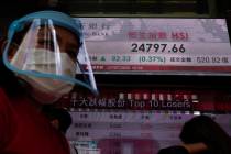 A man wearing a face mask and a shield walks past a bank's electronic board showing the Hong Ko ...