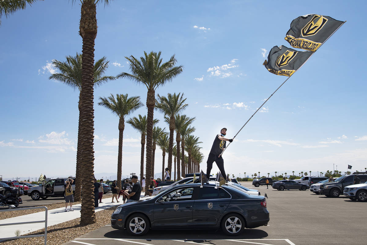 Matt Helfst waves a flag as he waits for the Golden Knights players to pass in buses as they le ...