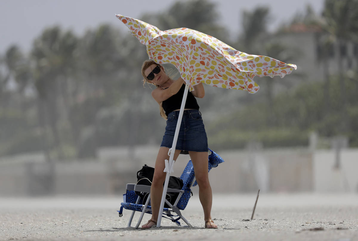 A beach goer attempts to set up a beach umbrella, Saturday, Aug. 1, 2020, in Palm Beach, Fla. H ...
