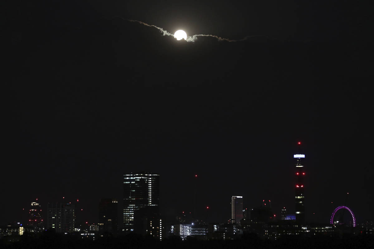 The full moon of August, known as the Sturgeon Moon, is partially seen from behind clouds above ...