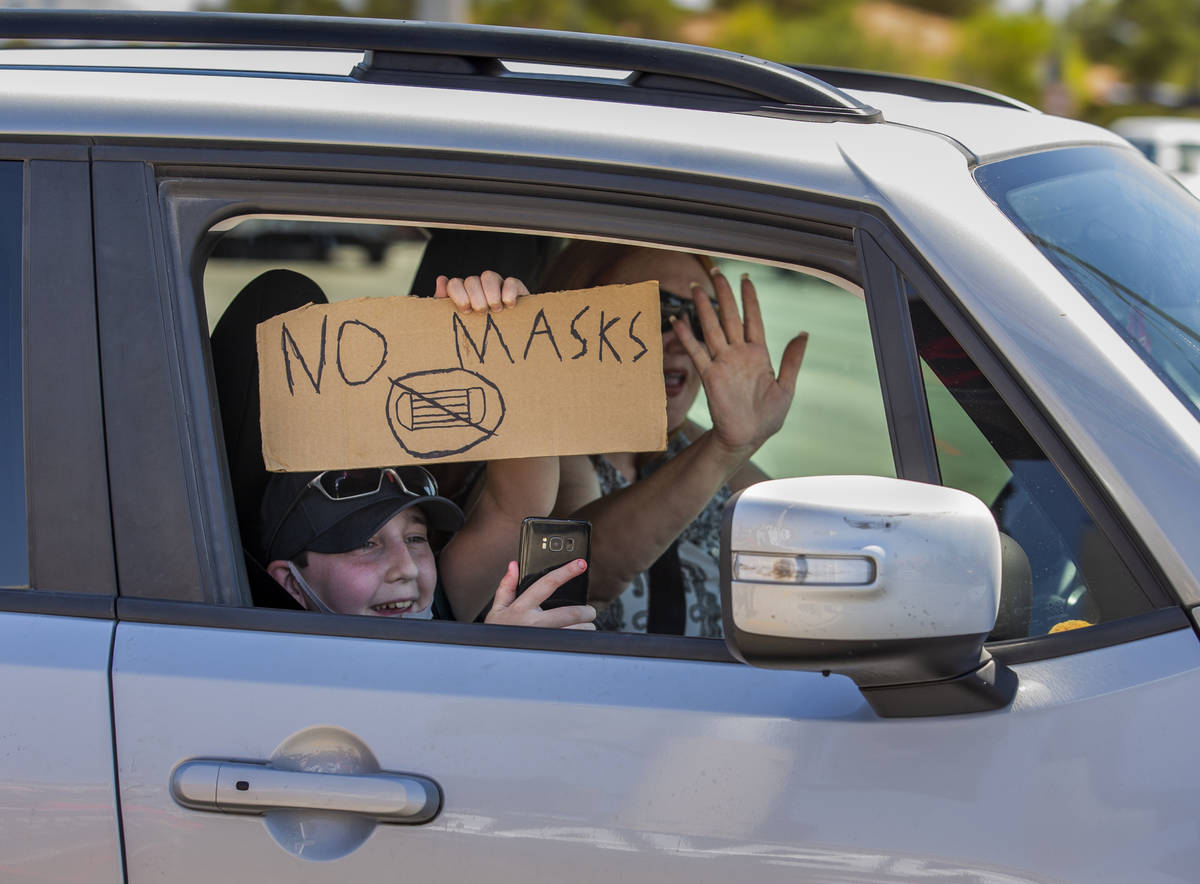 A passenger with sign and driver show their support as they pass by a No Mask Nevada rally to o ...