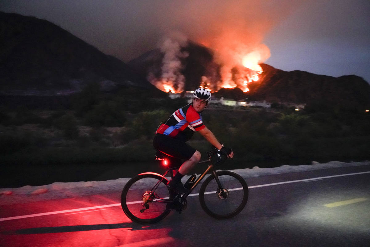 A cyclist rides along a trail as the Ranch Fire burns, Thursday, Aug. 13, 2020, in Azusa, Calif ...