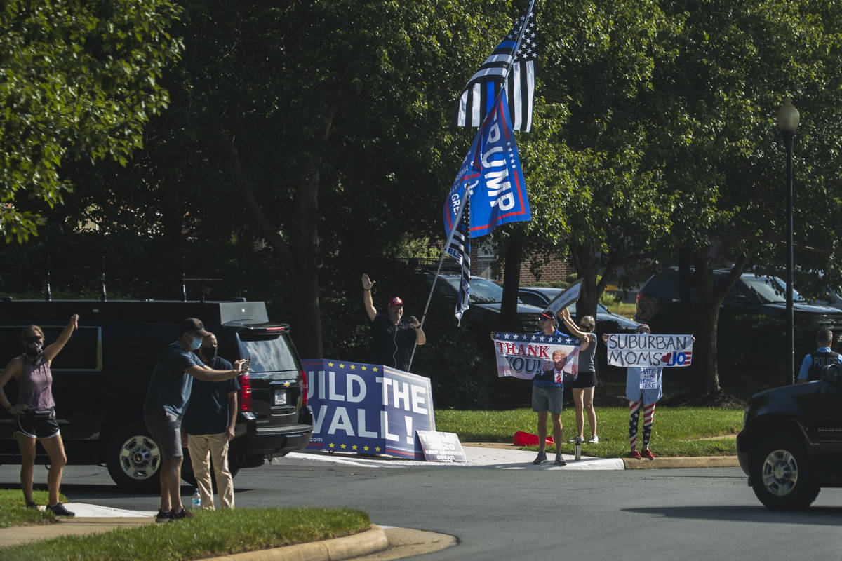 Protesters and supporters of President Donald Trump wave banners as the president's motorcade e ...