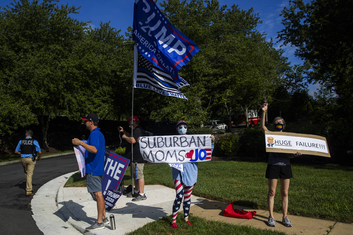 Protesters and supporters of President Donald Trump wave banners as the president's motorcade e ...