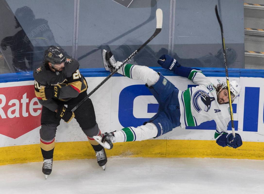 Vegas Golden Knights' Chandler Stephenson (20) checks Vancouver Canucks' Christopher Tanev (8) ...