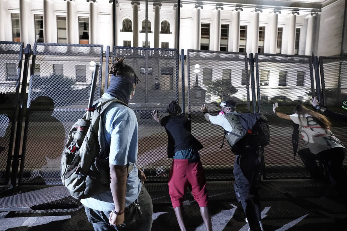 People try to push over protective fencing Tuesday, Aug. 25, 2020 in Kenosha, Wis. Anger over t ...