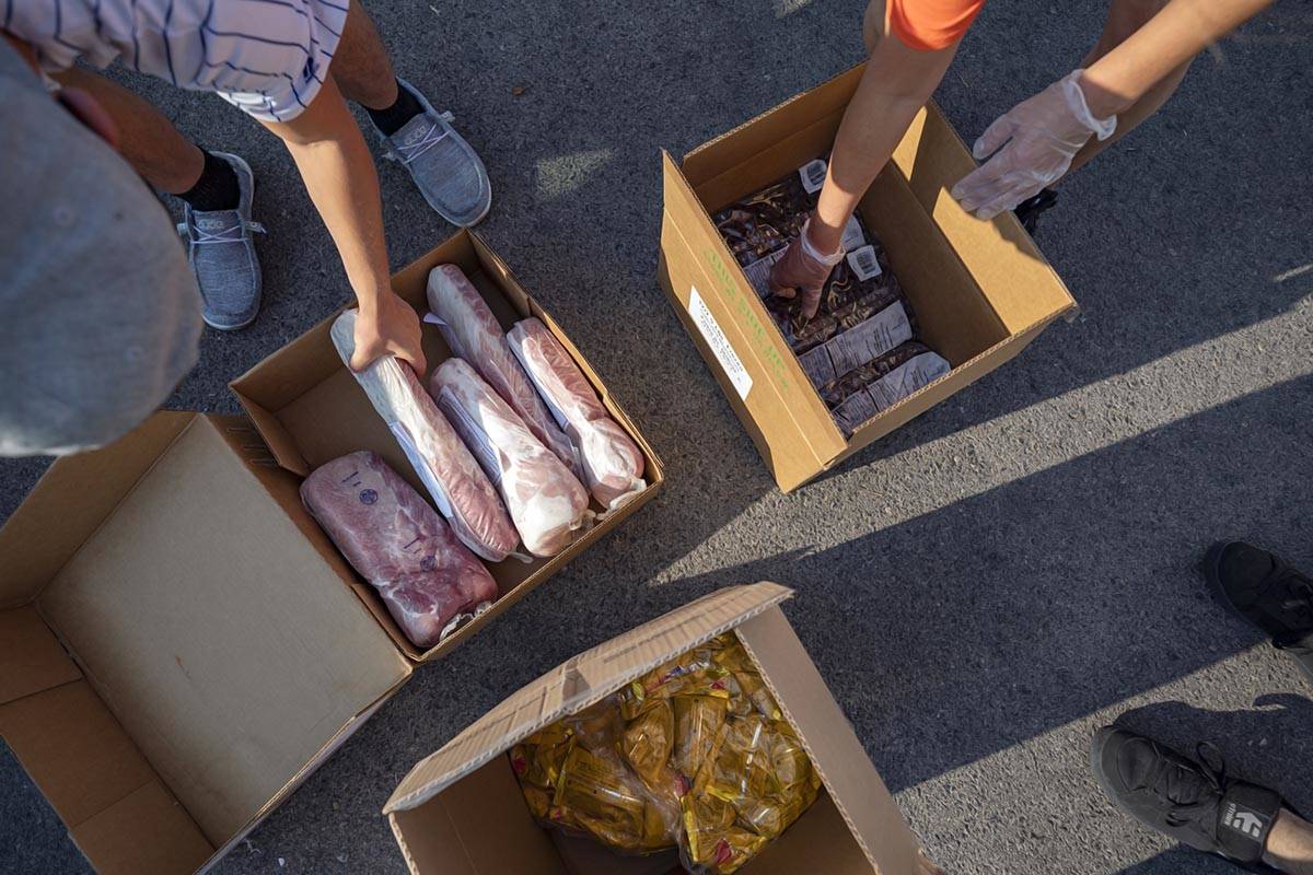 Three Square Food Bank volunteers grab frozen pork tenderloin, frozen blueberries and sack pack ...