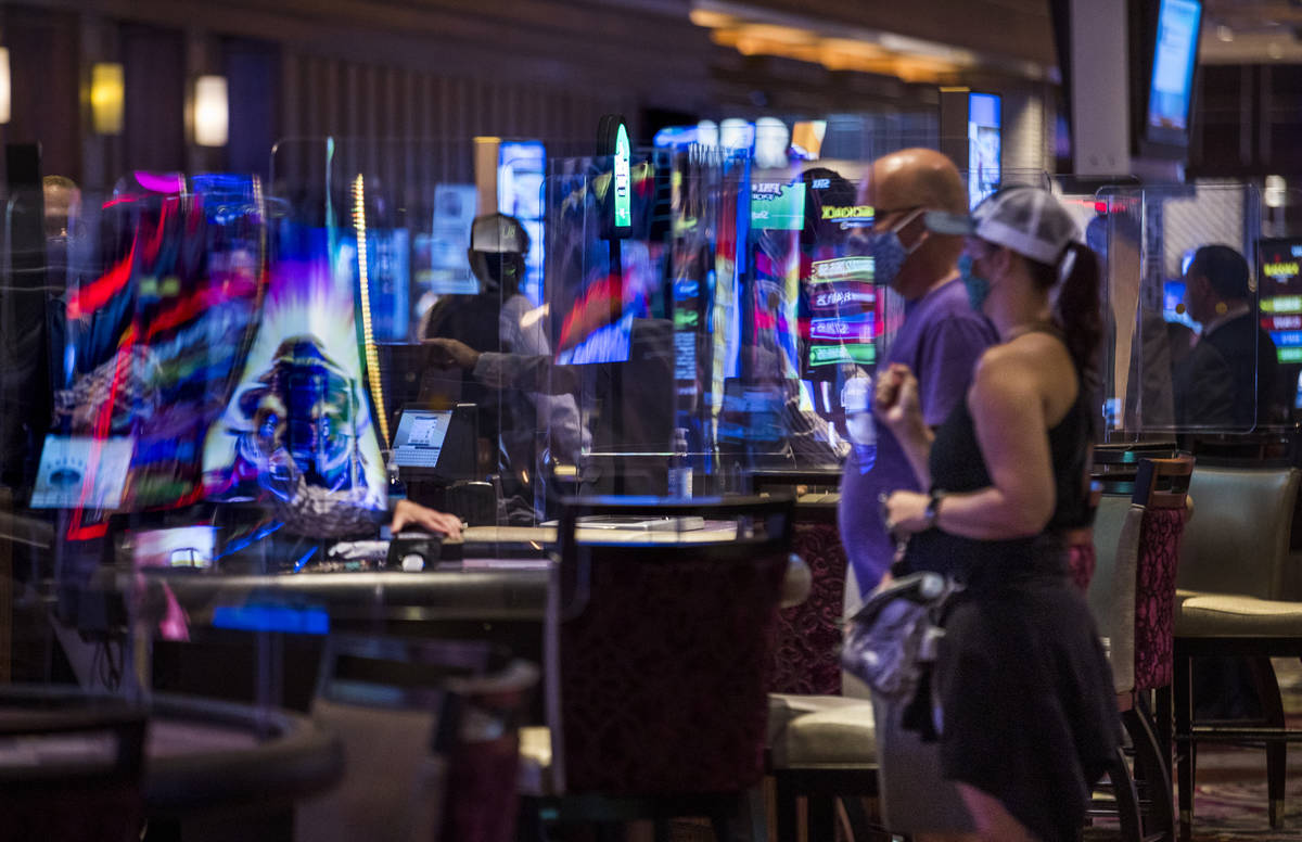 Guests approach a table game as the plexiglass reflects the electronic lights in the casino as ...