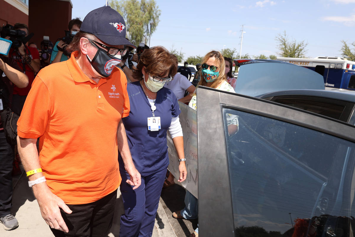 Paramedic John Foster, left, a recovered COVID-19 patient, gets assistance to his ride by Regis ...