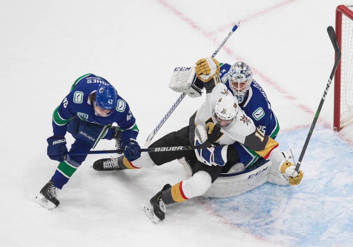 Vegas Golden Knights' Nicolas Roy (10) falls over Vancouver Canucks goalie Jacob Markstrom (25) ...