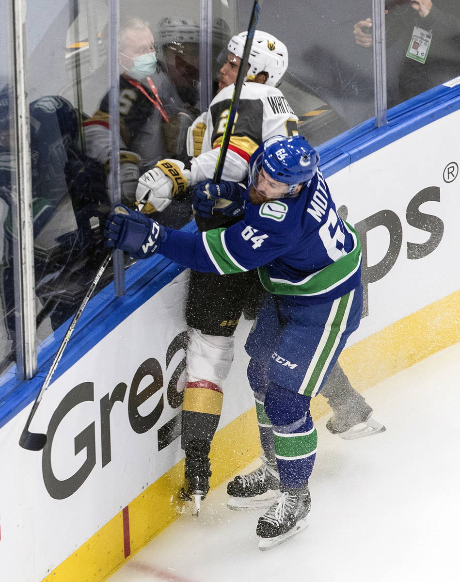 Vegas Golden Knights' Zach Whitecloud (2) is checked by Vancouver Canucks' Tyler Motte (64) dur ...
