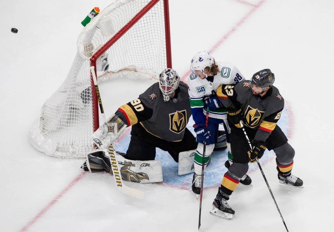 Vancouver Canucks' Adam Gaudette (88) and Alec Martinez (23) battle in front as Vegas Golden Kn ...