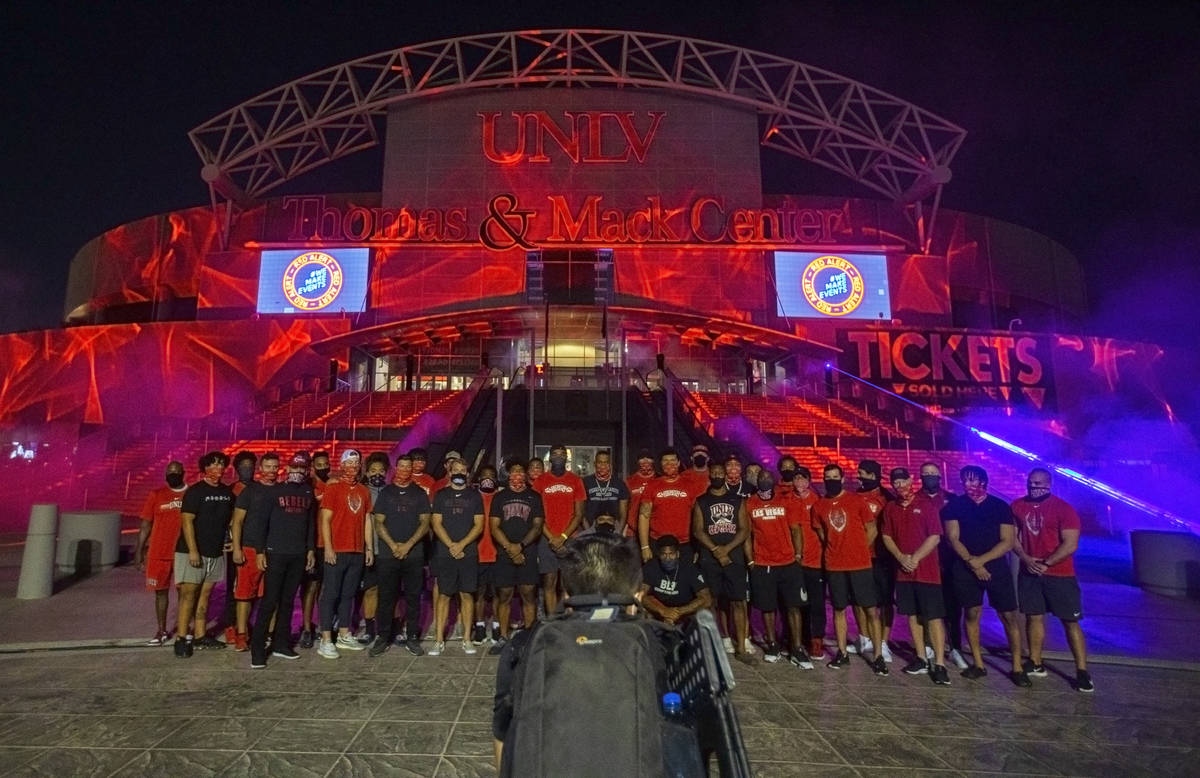 A group of UNLV football players, including head coach Marcus Arroyo, stand in front of a glowi ...