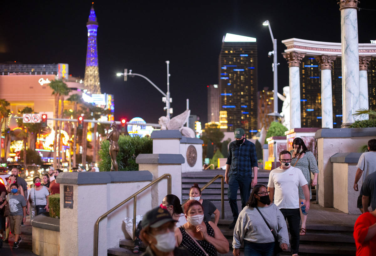 Some visitors wore masks while walking past Caesars Palace on the Strip while others refrained ...