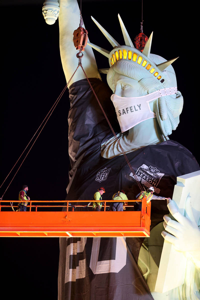 Workers install a a Las Vegas Raiders jersey on the Statue of Liberty replica at New York-New Y ...