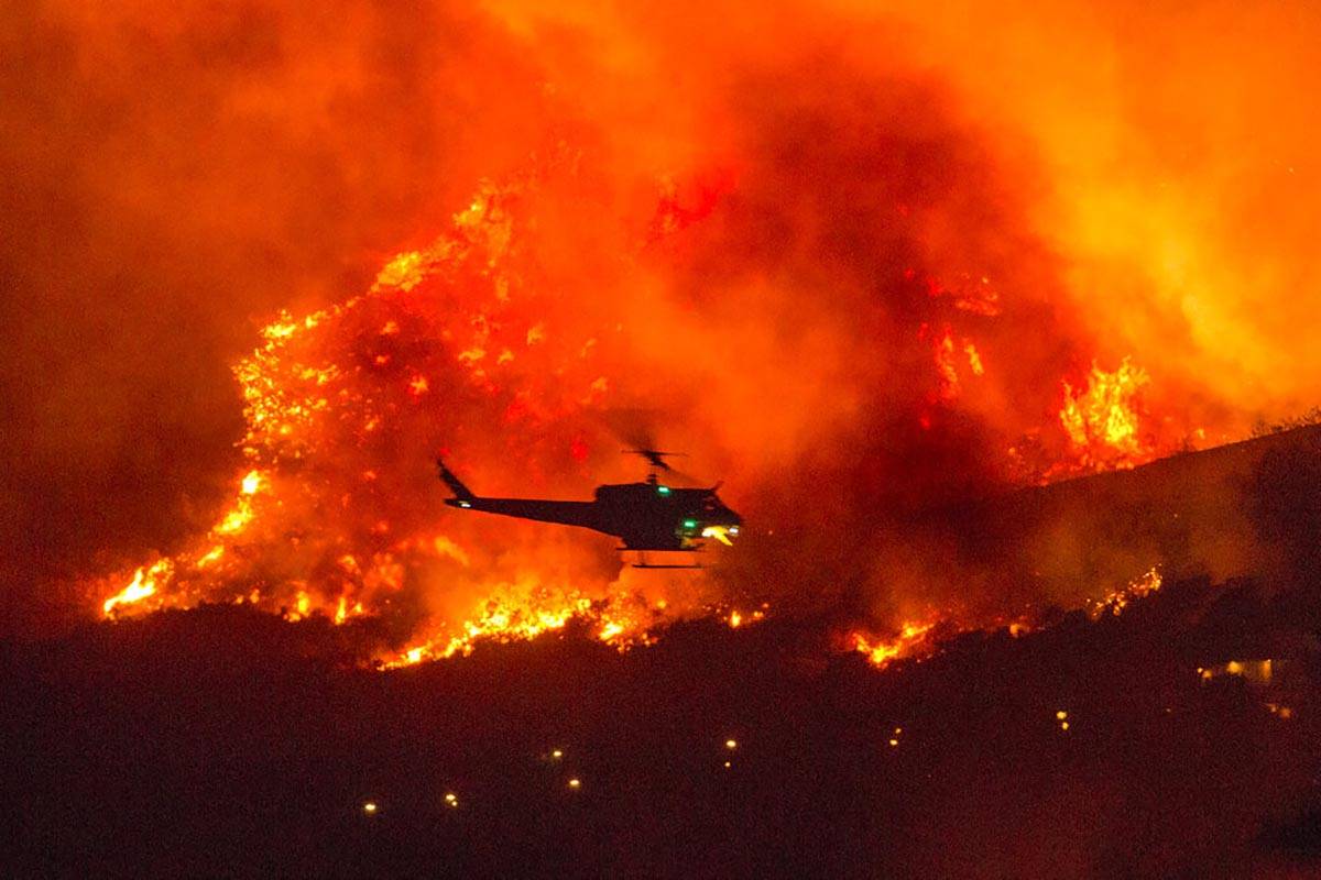 A helicopter prepares to drop water at a wildfire in Yucaipa, Calif., Saturday, Sept. 5, 2020. ...