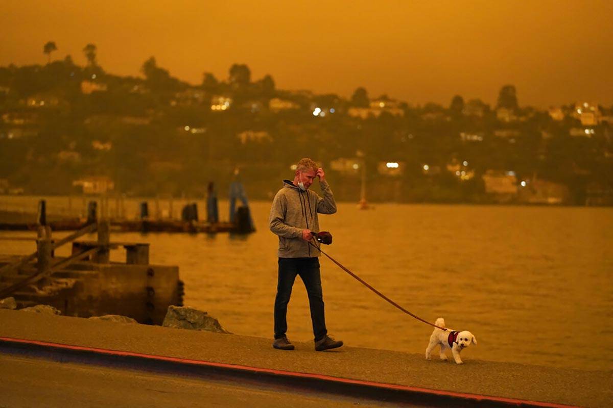 A man walks his dog along Bridgeway Avenue as smoke from wildfires darken the morning Wednesday ...