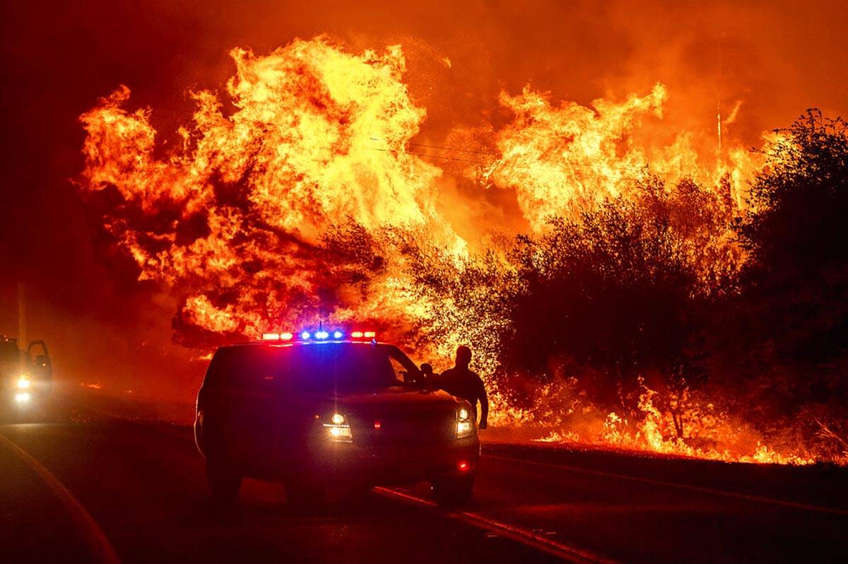 Flames lick above vehicles on Highway 162 as the Bear Fire burns in Oroville, Calif., on Wednes ...