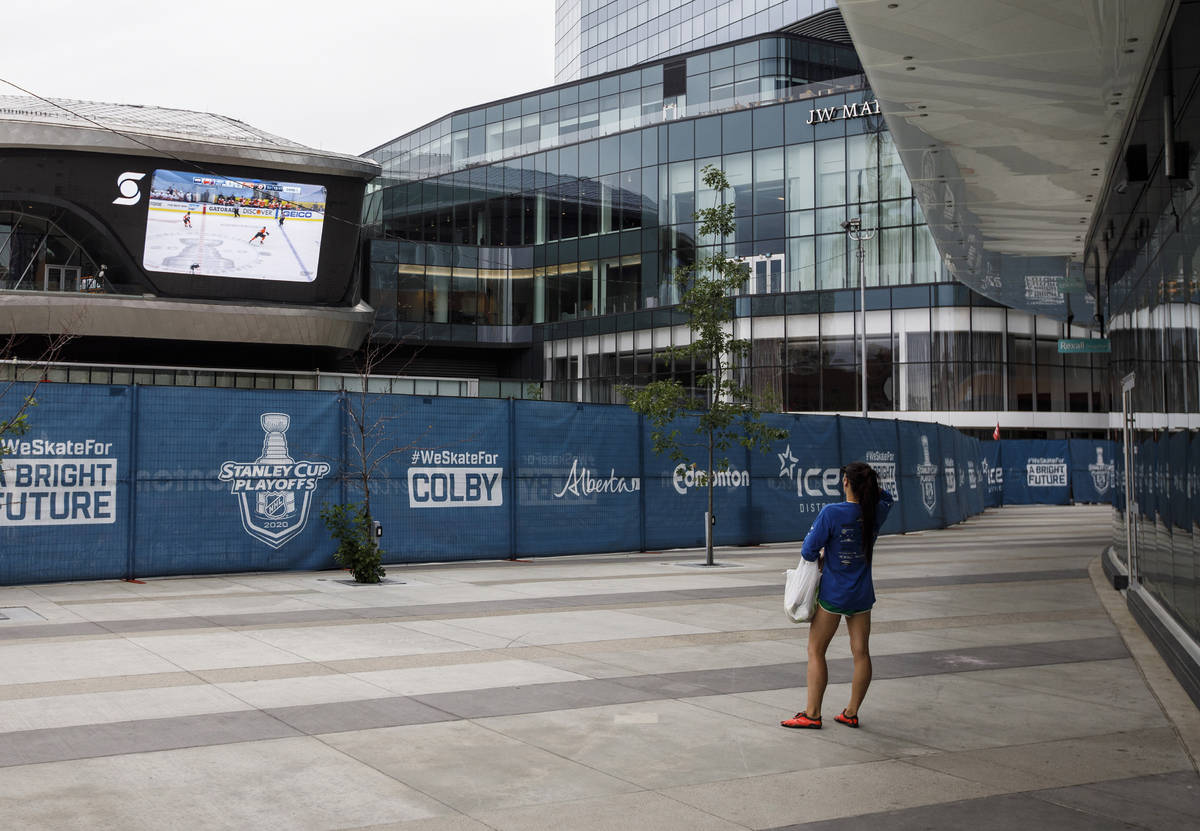 FILE - A woman watches a hockey game on the big screen just outside the bubble at the NHL Weste ...