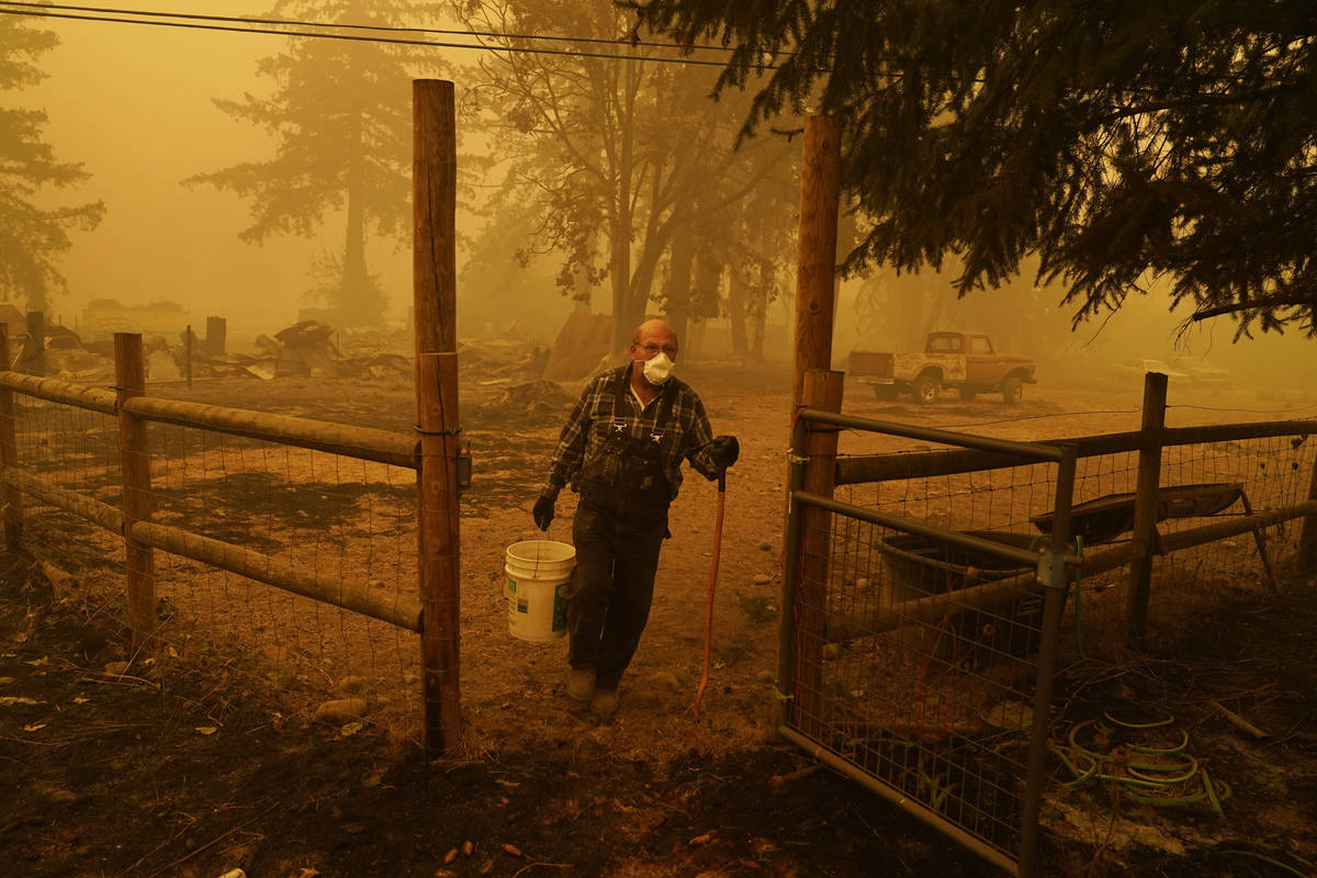 George Coble carries a bucket of water to put out a tree still smoldering on his property destr ...
