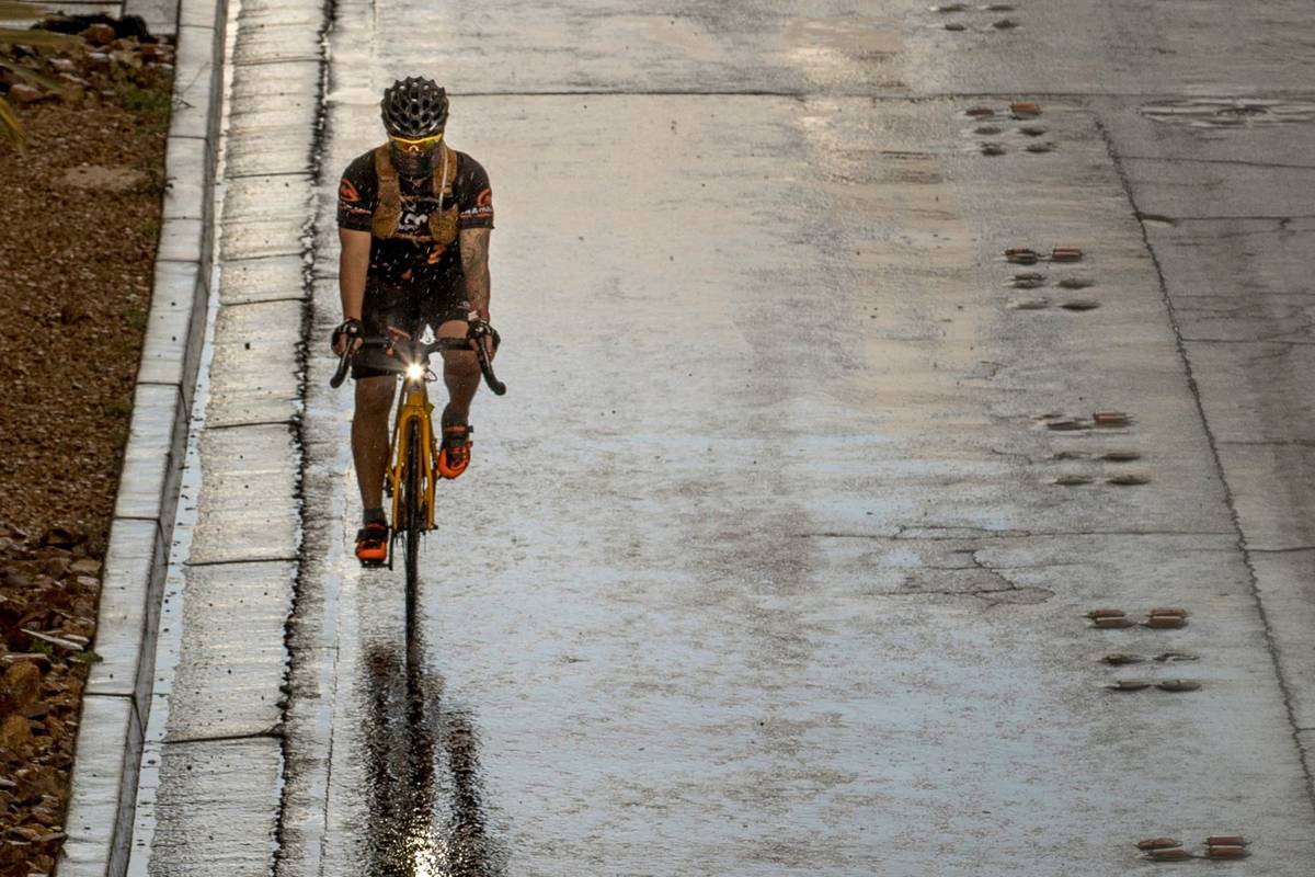 A cyclist wearing a face mask rides in the rain down the Las Vegas Strip past the Fashion Show ...