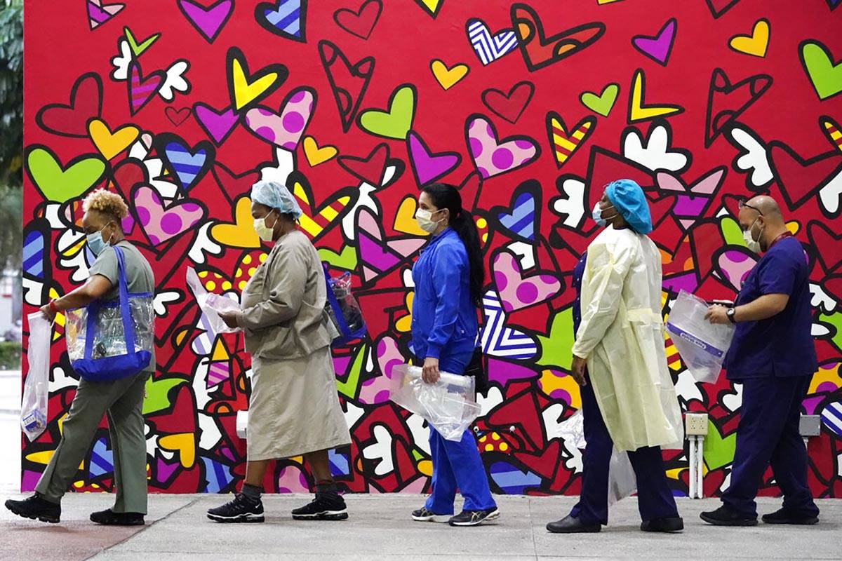 Healthcare workers line up for free personal protective equipment in front of a mural by artist ...