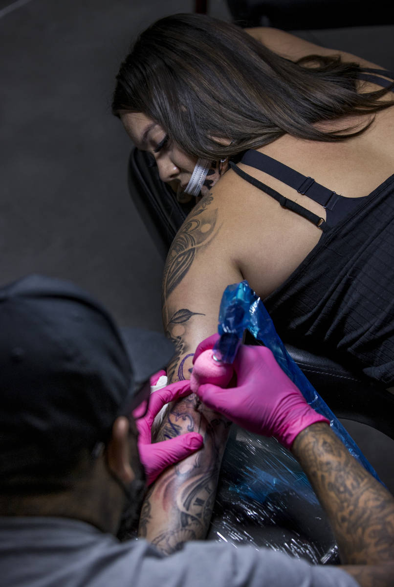 Natalia Baca, top, looks down at her tattoo and artist Sam Chacon as Route 91 shooting survivor ...
