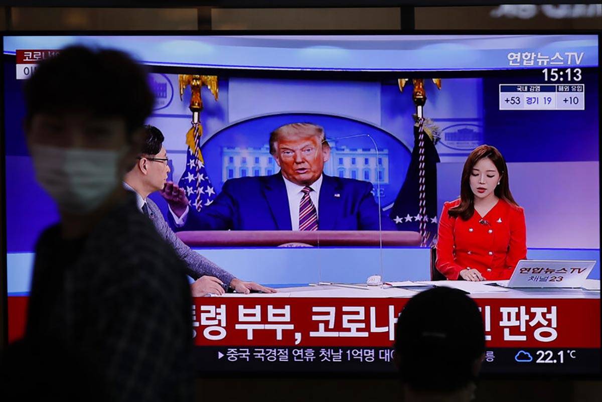 A man wearing a face mask walks near a TV screen reporting about U.S. President Donald Trump an ...