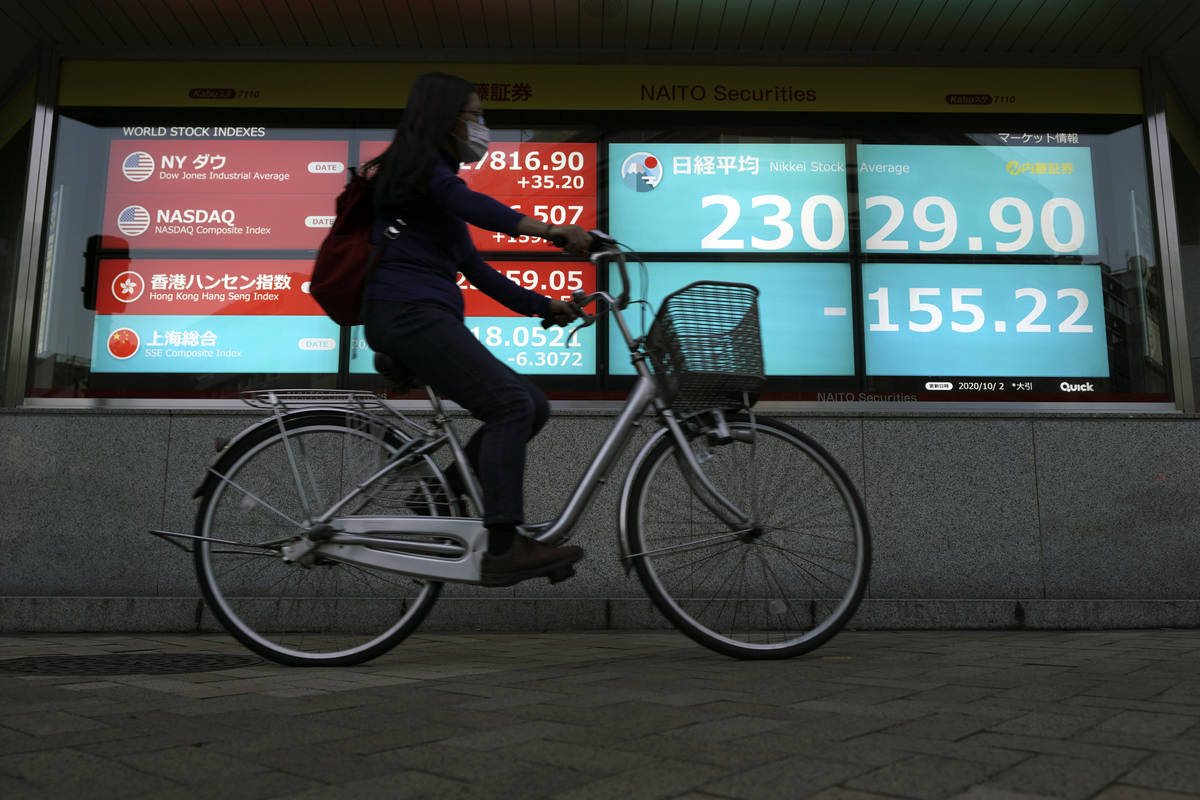 A woman rides a bicycle past an electronic stock board showing Japan's Nikkei 225 index at a se ...
