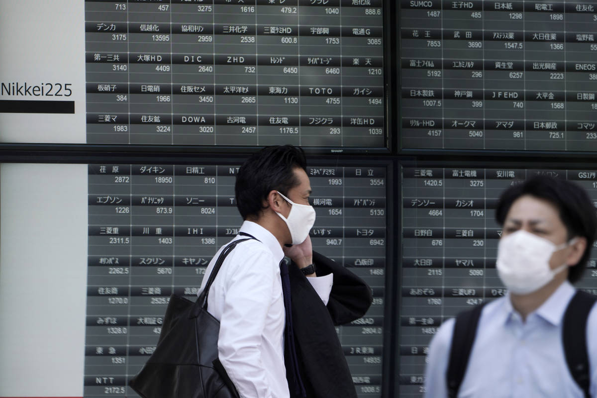 Men walk in front of an electronic stock board showing Japan's Nikkei 225 index at a securities ...