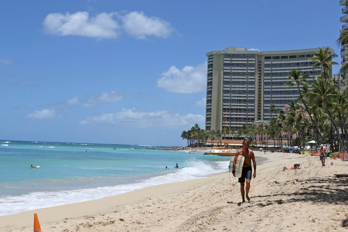 A surfer walks on a sparsely populated Waikiki Beach in Honolulu in June 2020. (AP Photo/Audrey ...