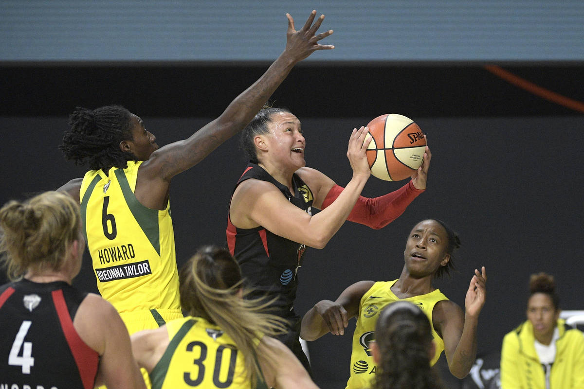 Las Vegas Aces guard Kayla McBride goes up to shoot between Seattle Storm forward Natasha Howar ...