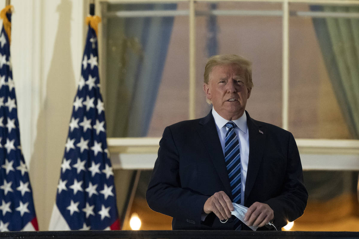 President Donald Trump removes his mask as he stands on the Blue Room Balcony upon returning to ...