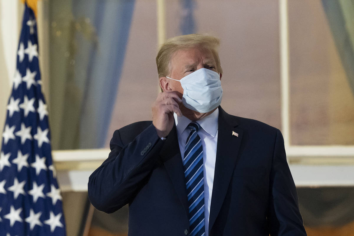 President Donald Trump removes his mask as he stands on the Blue Room Balcony upon returning to ...