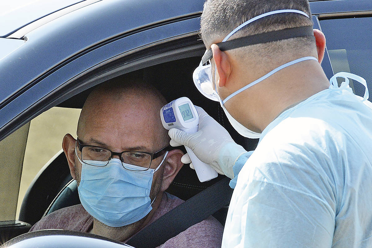U. S. Army, Arizona National Guard Pvt. Ronald Aguilar, right, takes the temperature of a man a ...