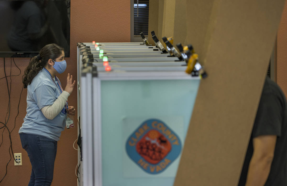 An elections worker gives instructions to a voter while in a booth with lights above showing th ...