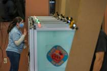 An elections worker gives instructions to a voter while in a booth with lights above showing th ...