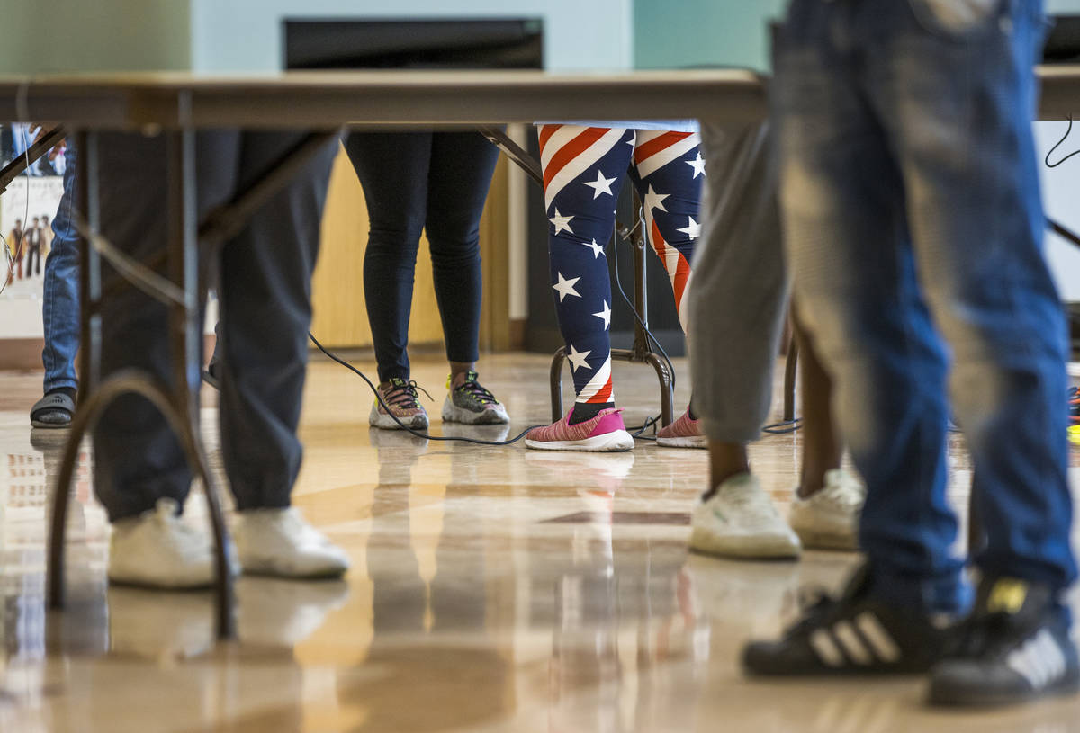 A volunteer in flag attire assists a voter at a voting machine at the Doolittle Community Cente ...