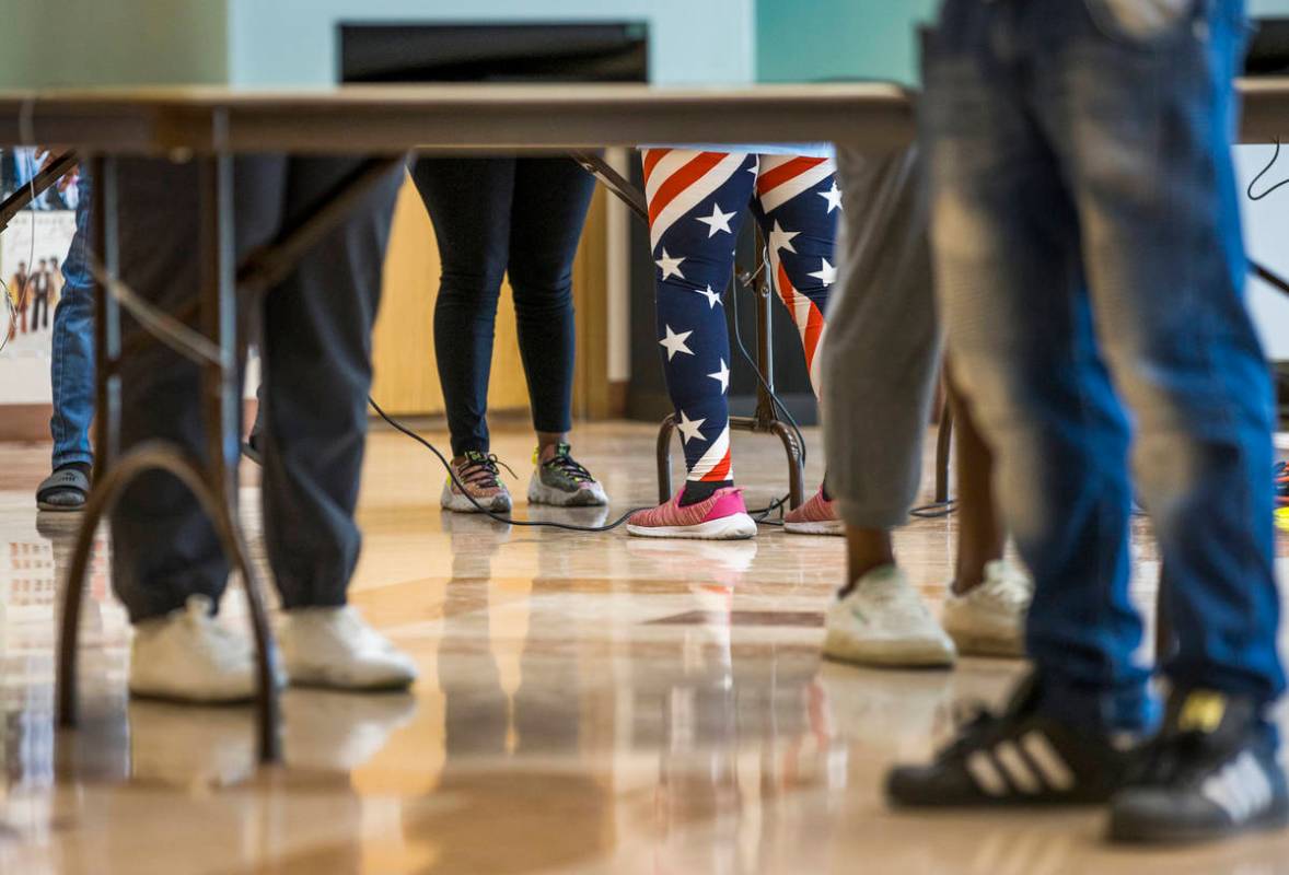 A volunteer in flag attire assists a voter at a voting machine at the Doolittle Community Cente ...