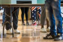A volunteer in flag attire assists a voter at a voting machine at the Doolittle Community Cente ...