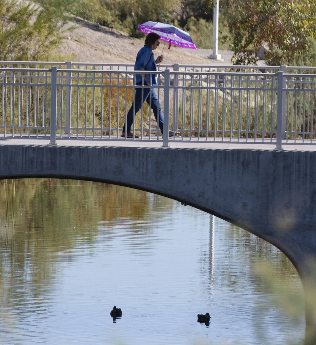 A woman holds an umbrella to protect herself from sun as she walks on pedestrian bridge at Corn ...