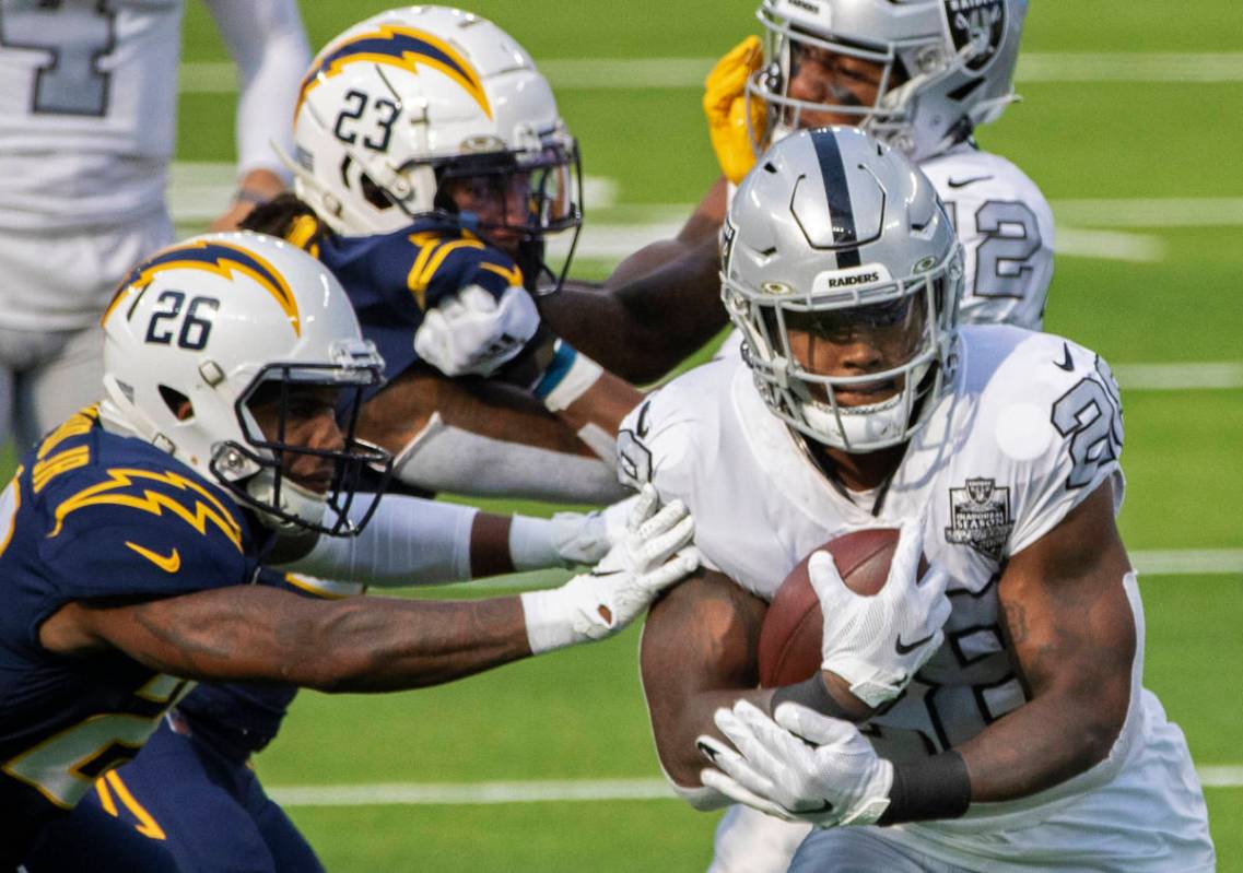 Las Vegas Raiders running back Josh Jacobs (28) breaks through the arm tackles of Los Angeles C ...