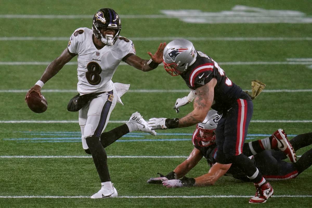 Baltimore Ravens quarterback Lamar Jackson, left, tries to elude New England Patriots defensive ...