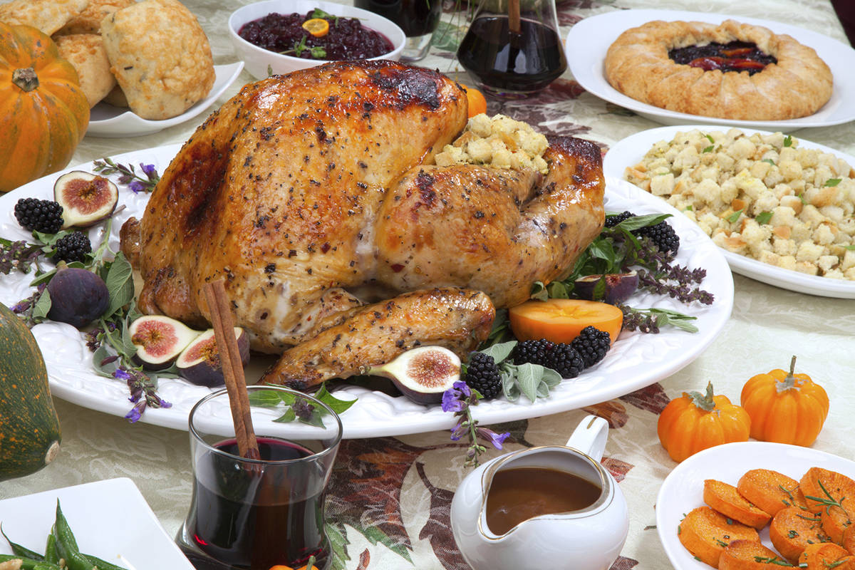 Dinner table with roasted Thanksgiving turkey is ready to feast. Turkey is garnished with fresh ...