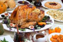Dinner table with roasted Thanksgiving turkey is ready to feast. Turkey is garnished with fresh ...