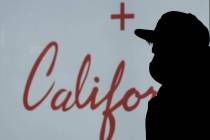 A Black Friday shopper wearing a face mask is silhouetted while waiting in line to enter a stor ...